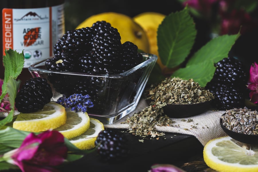 Fresh blackberries sit beside dried blackberry leaf, lavender, and lemon