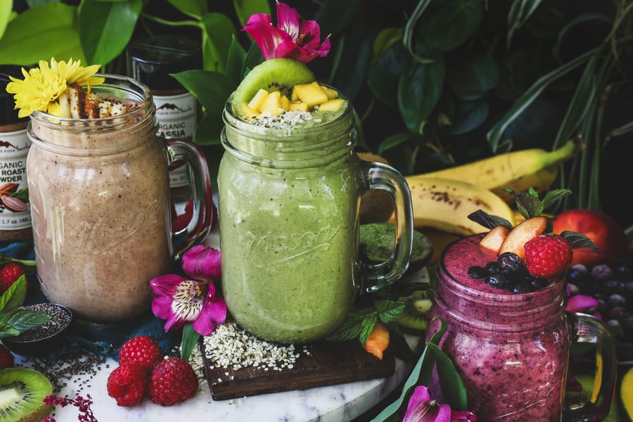 3 superfood smoothies sit out surrounded by fruit and other ingredients