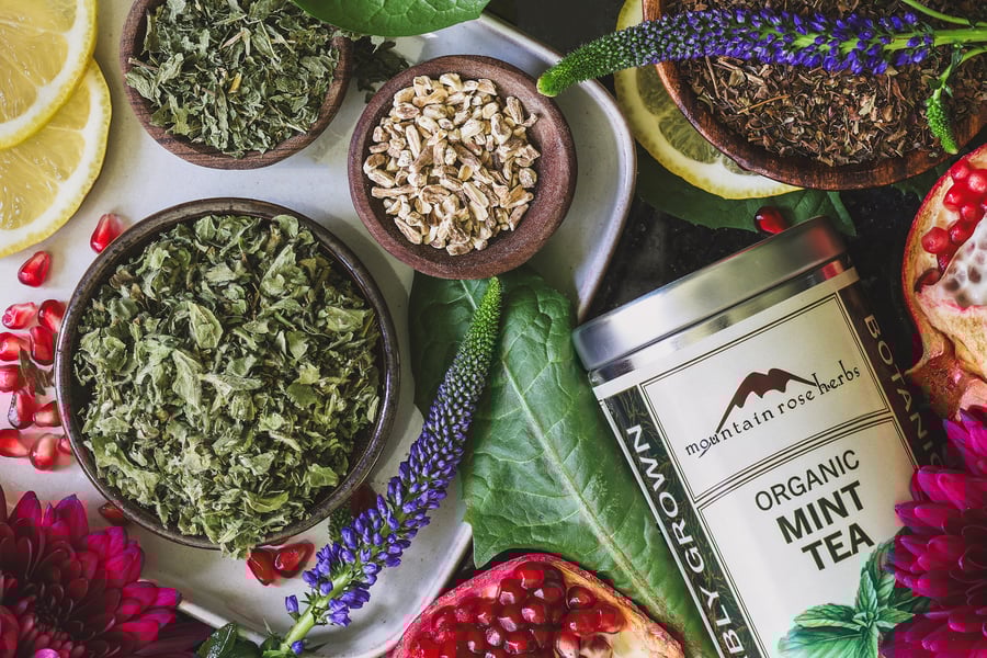 An overhead shot of dried herbs in small bowls and a tin of mint tea 