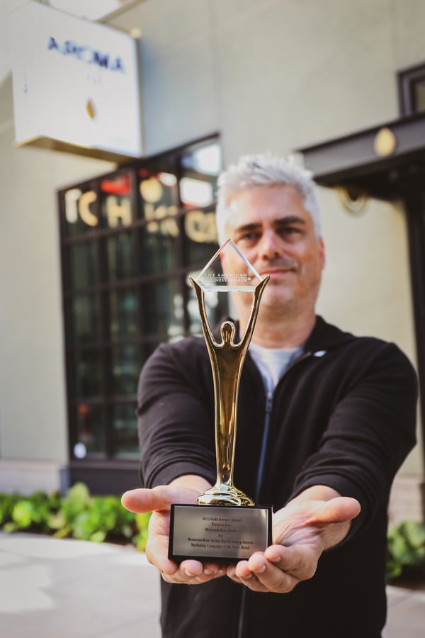 Creative Director, Thomas Dick, holding Stevie Award in front of the Mountain Rose Aroma Bar