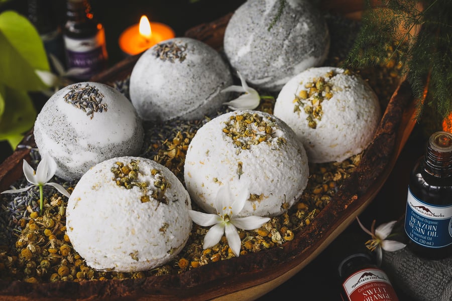 Bath bombs sit in a wooden bowl filled with chamomile and lavender flowers