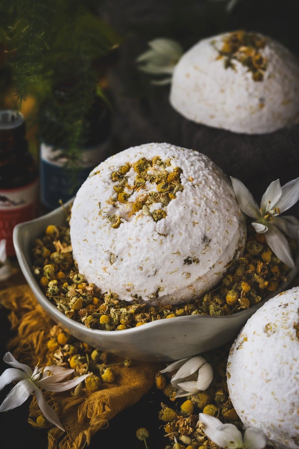 A sunshine bath bombs sits in a bowl of chamomile flowers