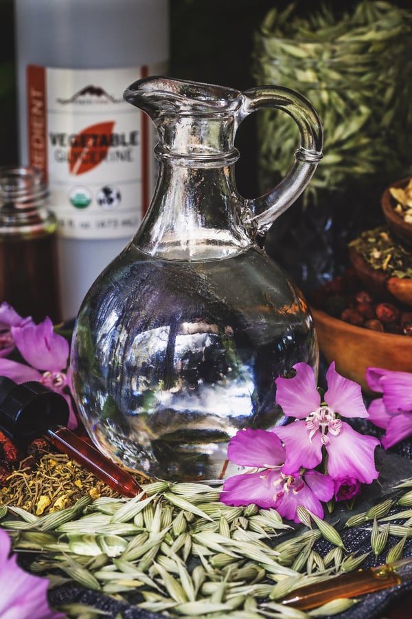 A jar of vegetable glycerine surrounded by herbs and flowers