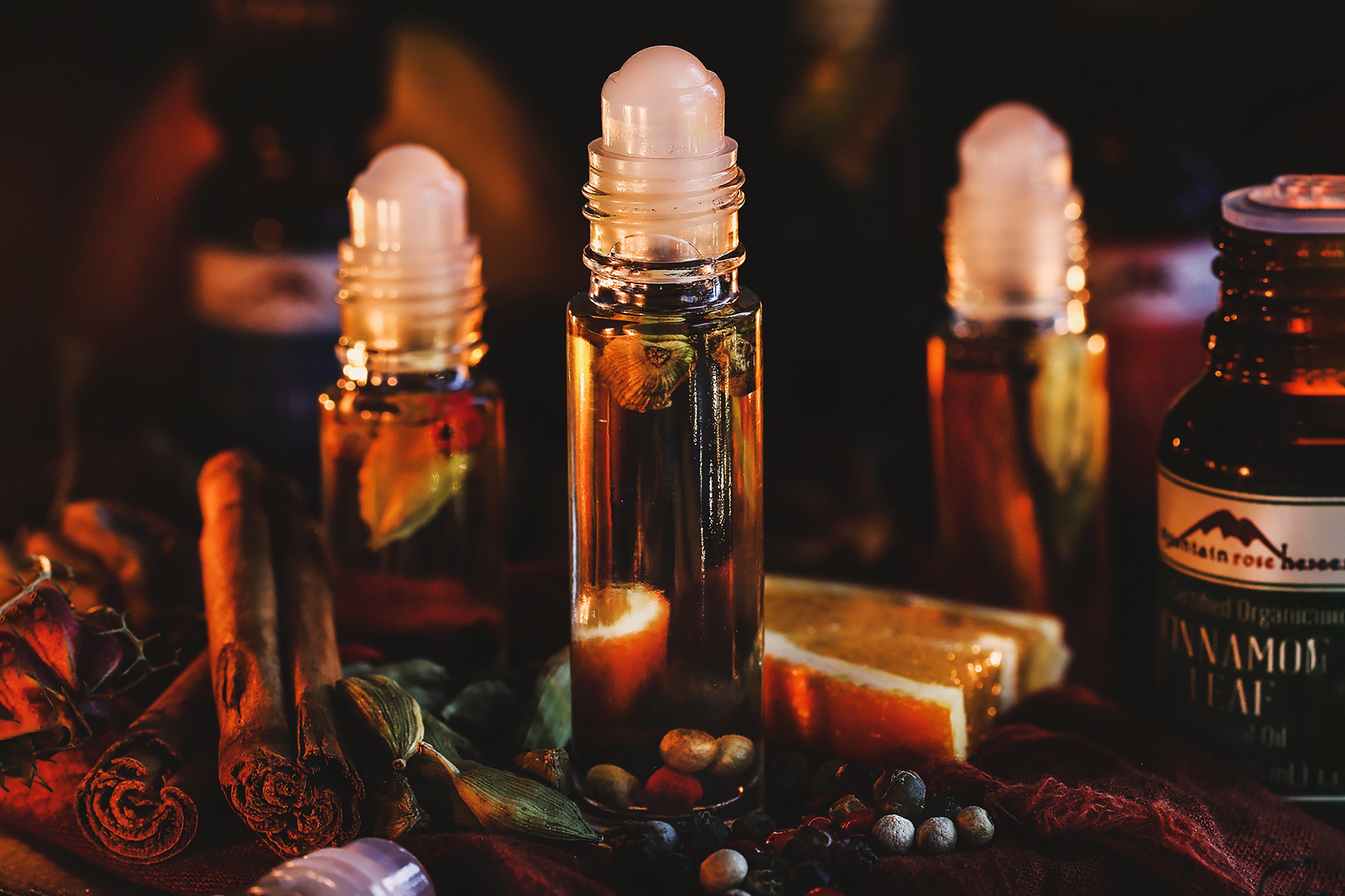 Close up photos of roll-top bottles filled with aromatic botanical and surrounded by essential oils and fresh cinnamon sticks. 