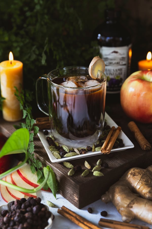 A sultry switchel chilling in a glass mug with ingredients around it