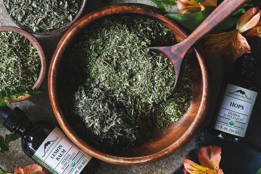 An overhead photo of a bowl with dried skullcap and lemon balm in it with hops and lemon balm extracts near it