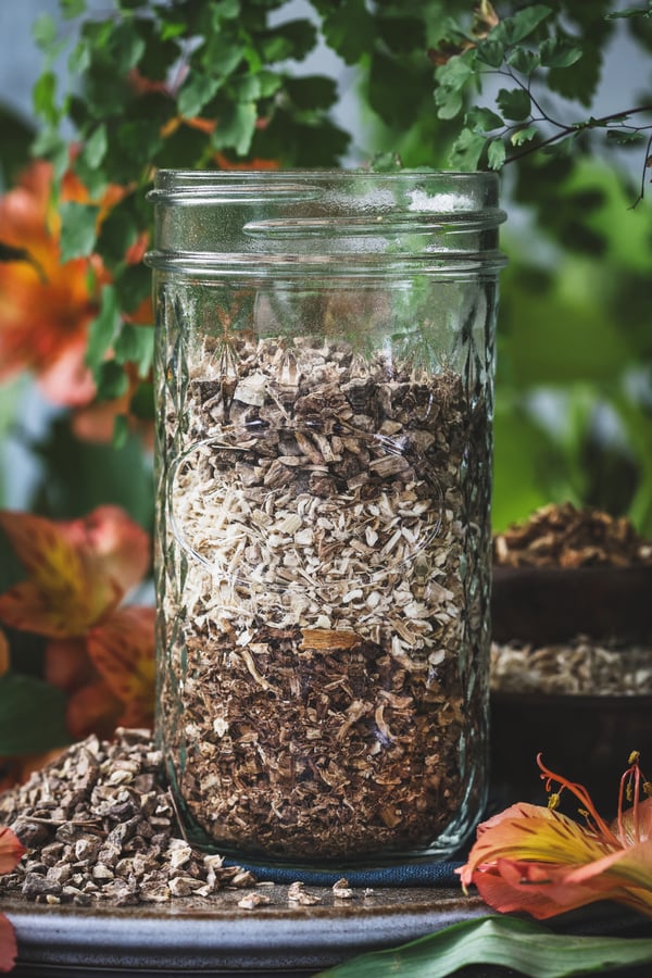 A glass jar with dried angelica, marshmallow, and burdock root in it