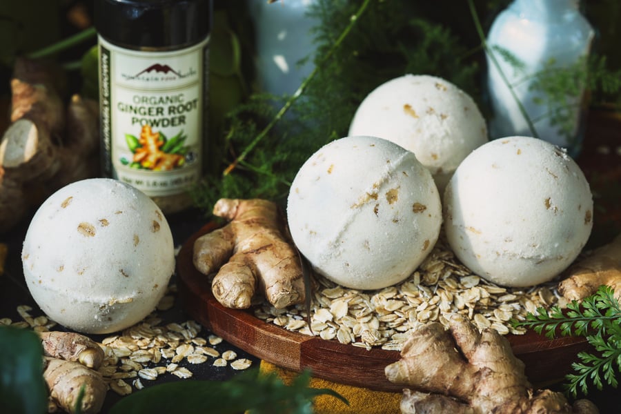 Bath bombs sit on rolled oats with ginger root and a bottle of ginger powder nearby