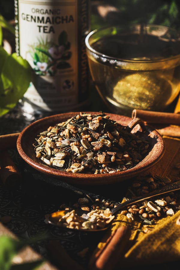 Green tea spice blend in a dish with ingredients and warm cup of tea in the background