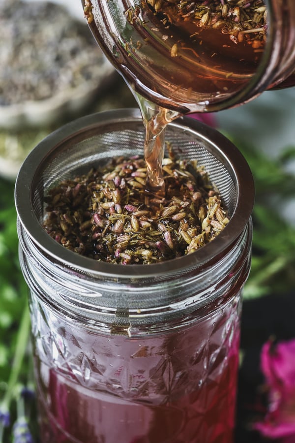 A close up shot of lavender-yarrow oxymel being strained into a jar