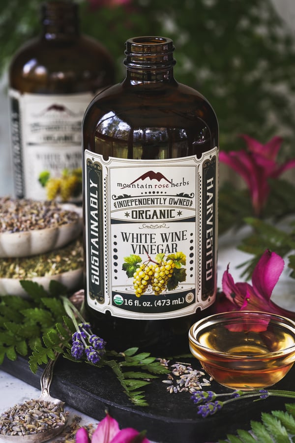 A bottle of white wine vinegar with oxymel herbs around it