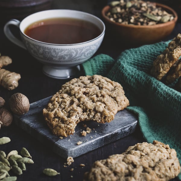 A freshly baked cookie sits beside a steamy cup of tea