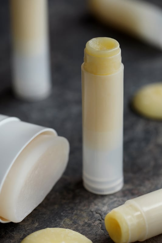 Lip balms and deodorants made with botanical body butters displayed with cocoa butter wafers around them. 