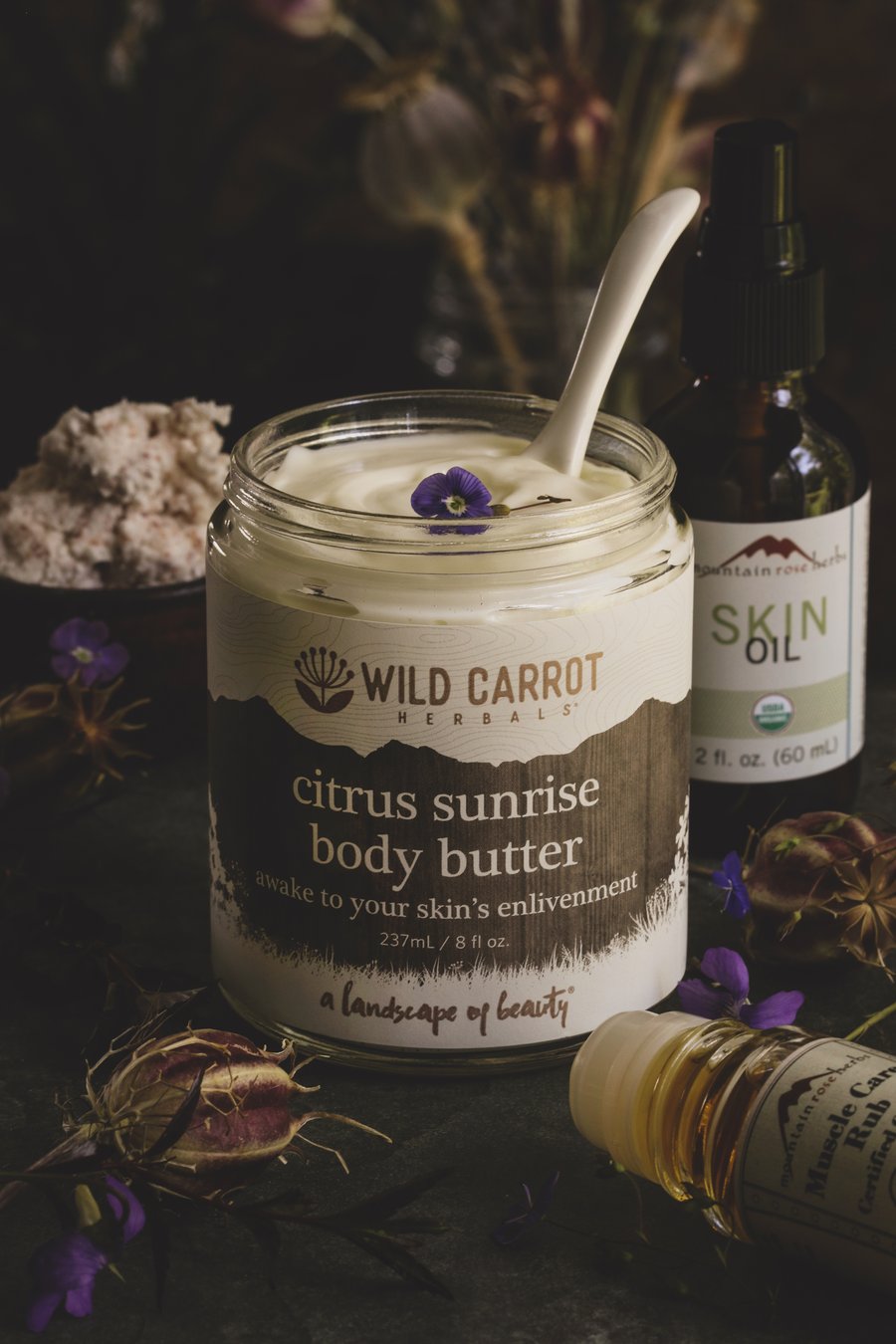Wild Carrot Citrus Sunrise body butter surrounded with other body care products.