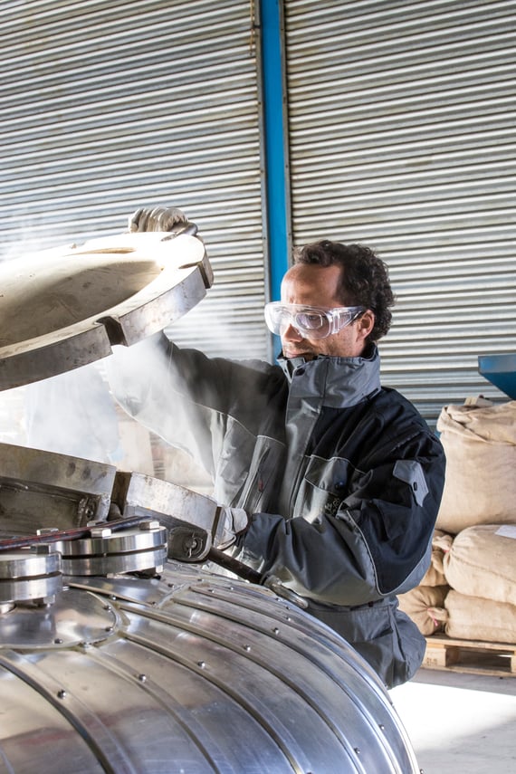 Essential oil distiller in safety glasses looking into stainless steel still