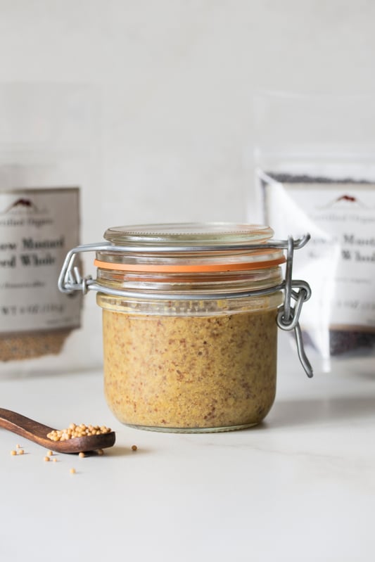 Pantry jar full of mustard with display of ingredients used to make it. 