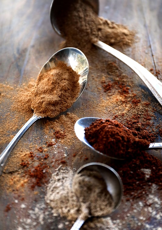 Colorful powdered herbs spilling out of spoons on a rustic wooden table. 