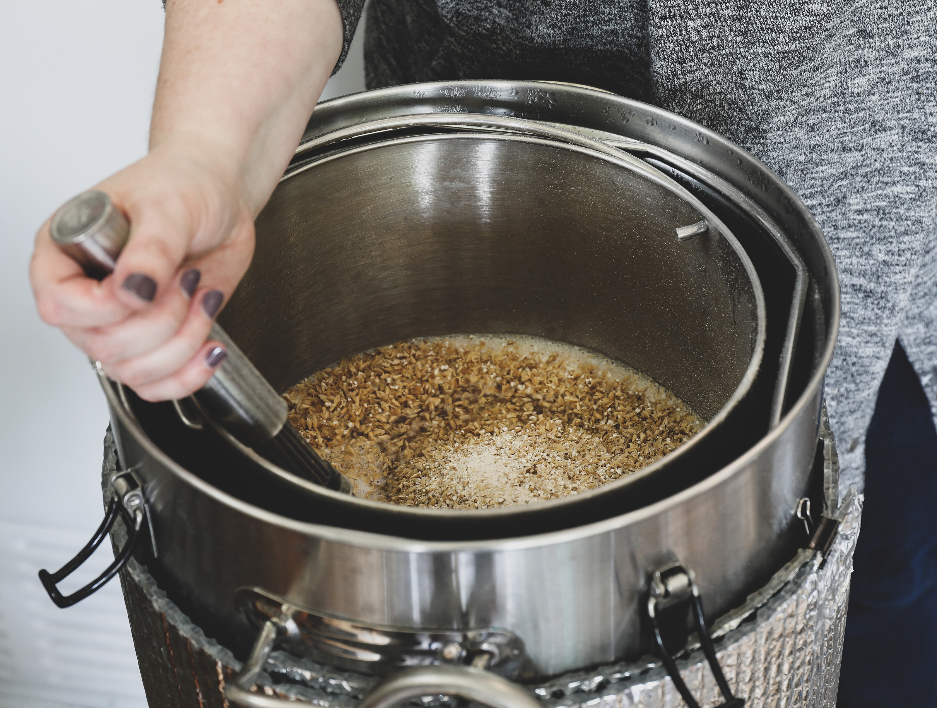 Hand stirring grain in pots with hot water for herbal beer brewing
