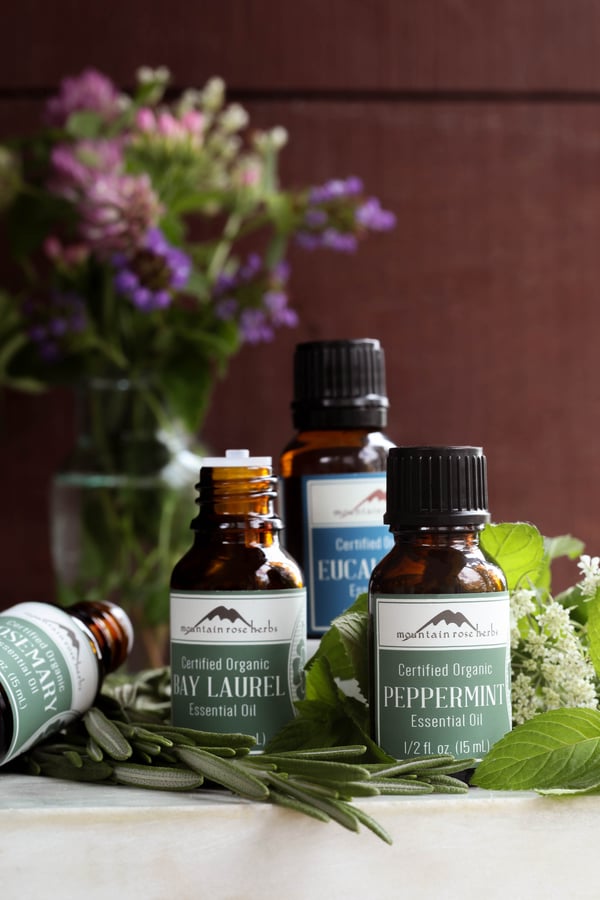 Rosemary, Bay Laure, Eucalyptus, and Peppermint Essential oils surrounded by fresh botanicals.