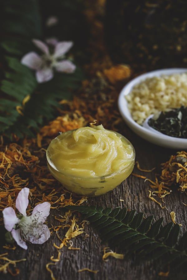 Bowl of natural herbal diaper rash ointment surrounded by botanical ingredients.