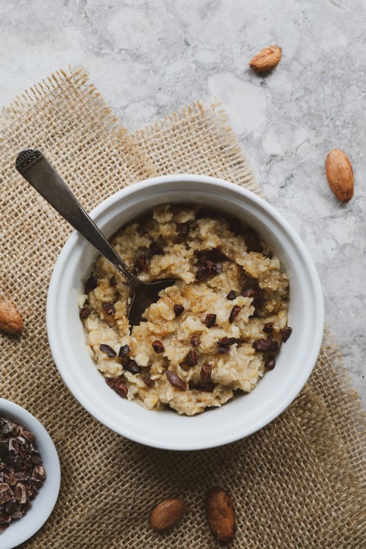 Cacao nibs in bowl of hot breakfast cereal surrounded by whole nibs