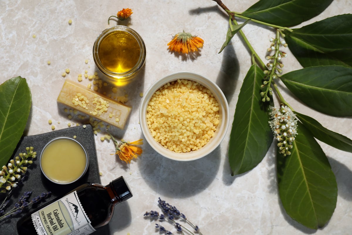 Calendula salve ingredients like beeswax pastilles, herbal oil, and fresh lavender.