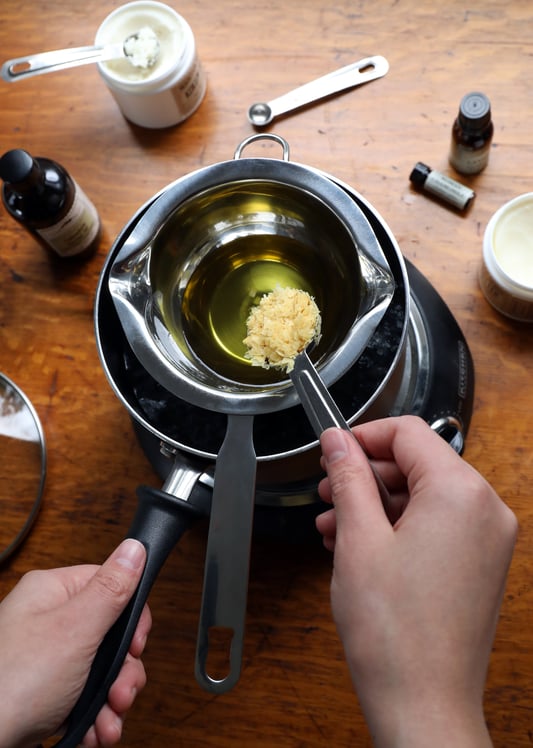 Hand pouring carnauba wax into double boiler for salve recipe making