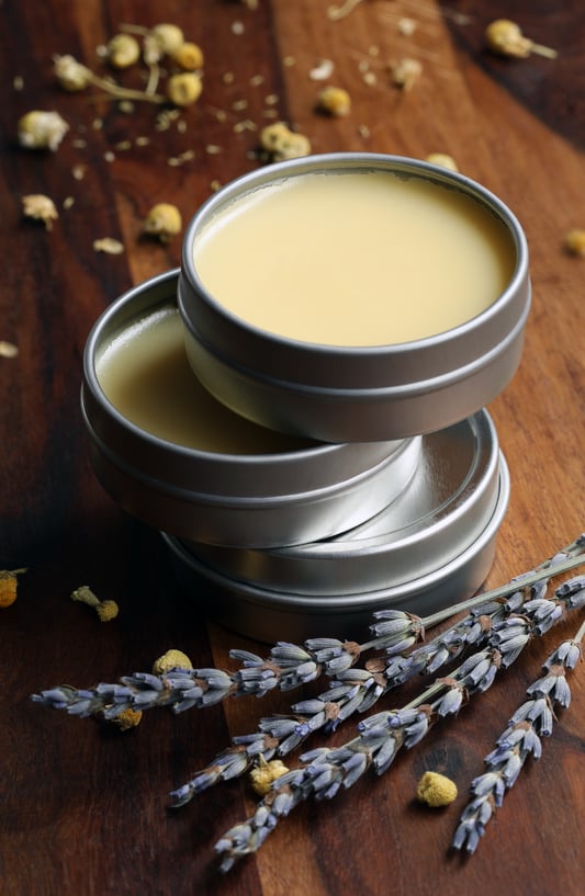 stacked tins of calendula vegan salve on wooden surface with dried herbs