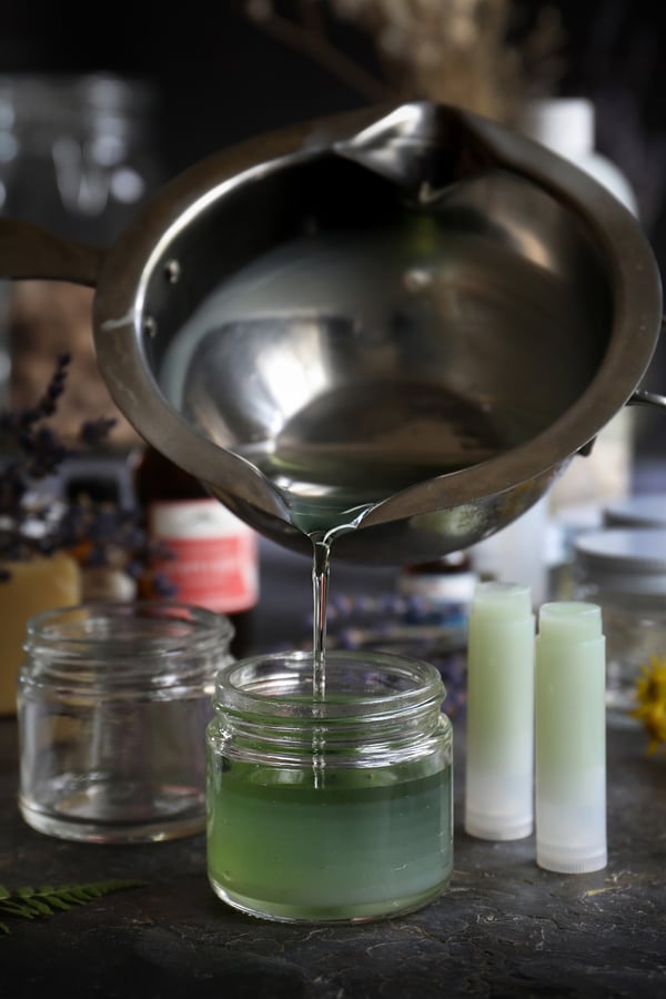 Liquid perfume blend pouring from a double boiler into a jar to harden to make solid perfume.