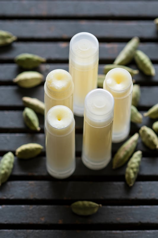 Lip balm in tubes with cardamom pods displayed on wood. 