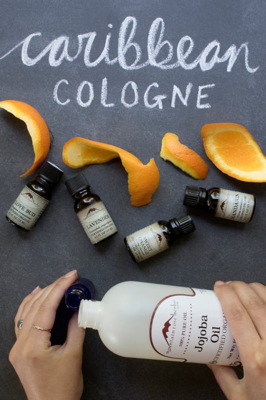 Hands pouring jojoba oil into glass bottle with citrus peels Caribbean Cologne essential oil fragrance recipe