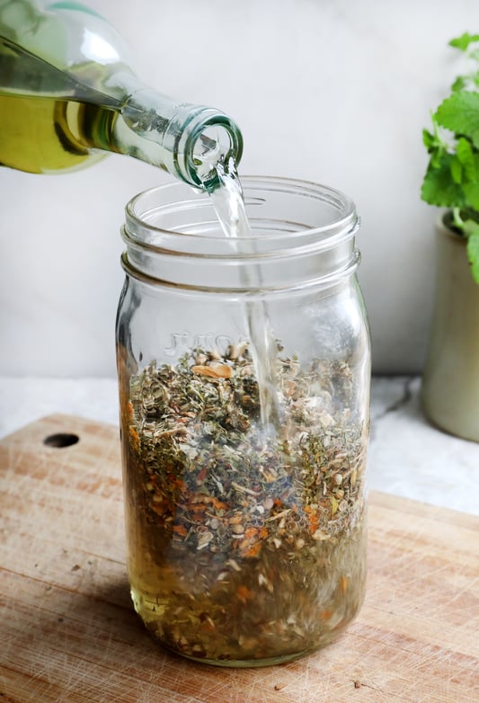 Pouring wine into a canning jar filled with dried herbs to make Carmelite water with lemon balm