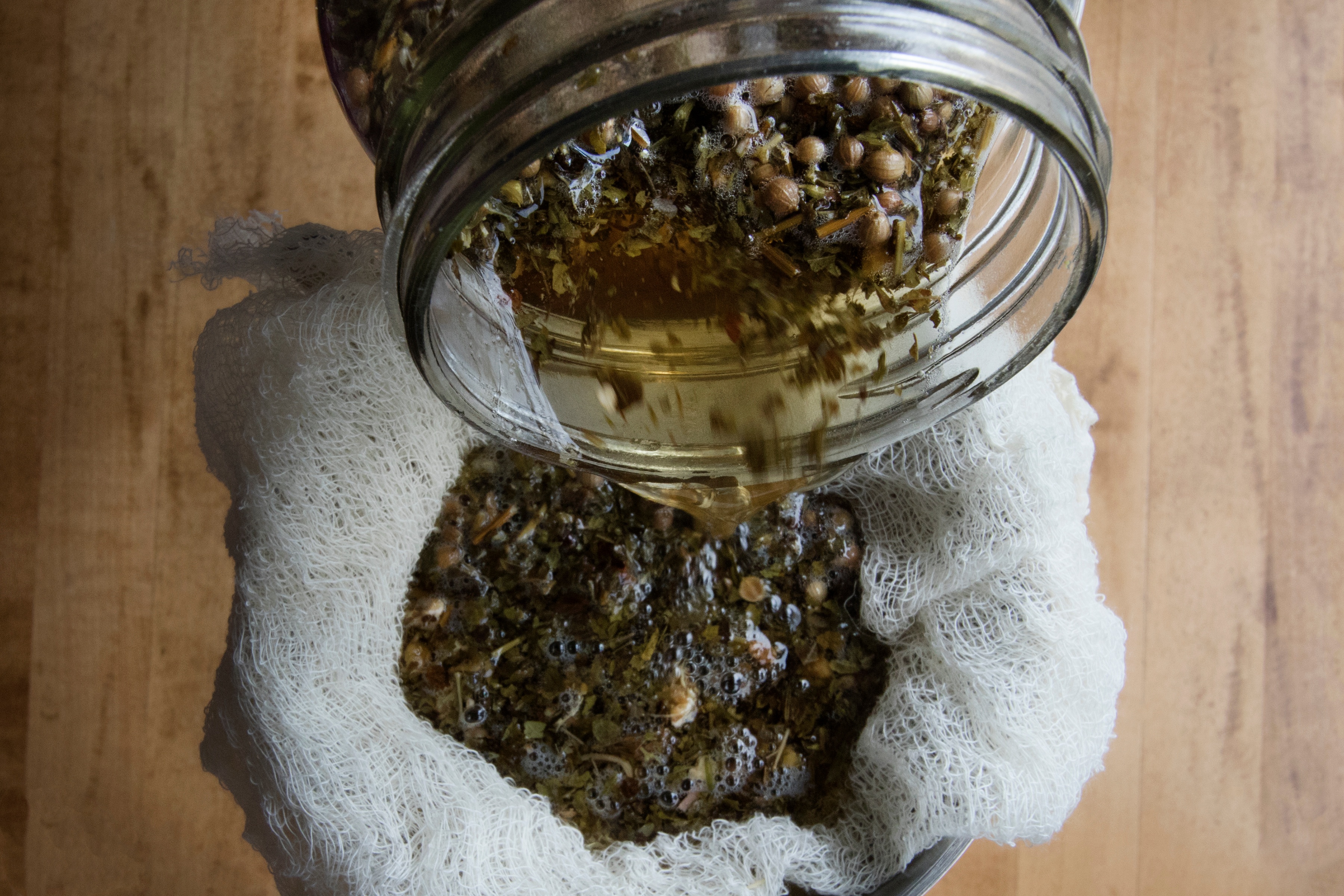 Pantry jar pouring Carmelite water and herbs through cheesecloth to strain