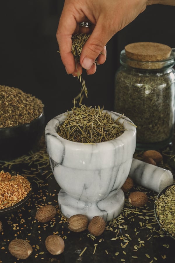 Hand dropping rosemary leaves into mortar and pestle. 