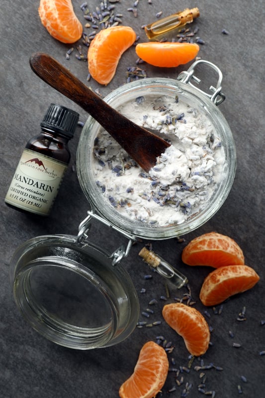 Herbal carpet deodorizing powder in glass mason jar surrounded by mandarin orange slices and mandarin essential oil.