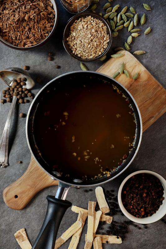 Pan of astragalus chai tea decoction with bowls of spices.
