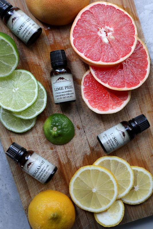 Lime peel essential oil, bergamot essential oil, lemon essential oil, and grapefruit essential oil on wooden chopping board with fresh fruit