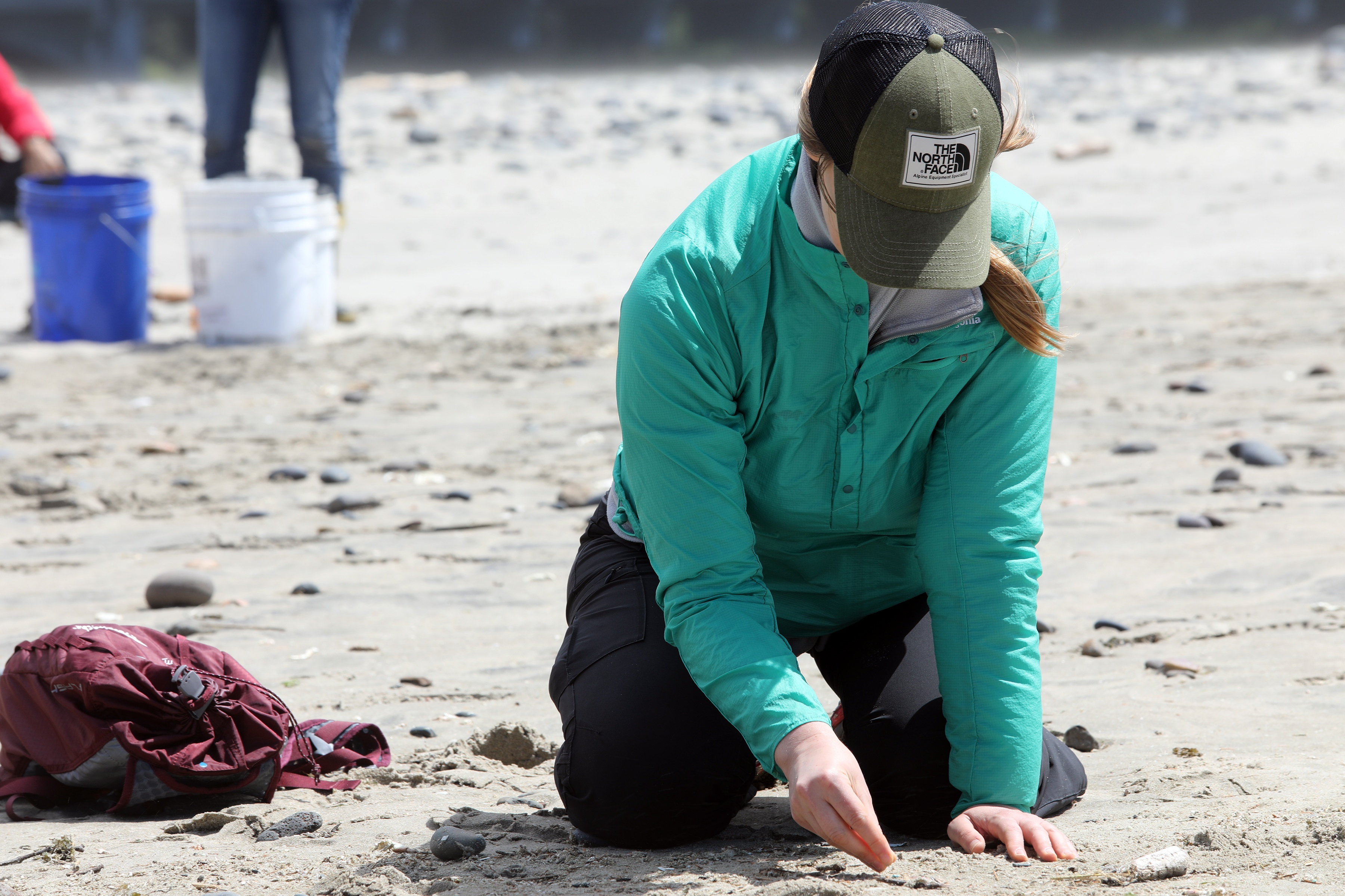 Person kneeling on sand to pick up trash during a beach cleanup