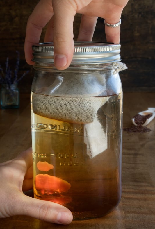 Mason jar with cotton tea bag in water with hands tightening lid.