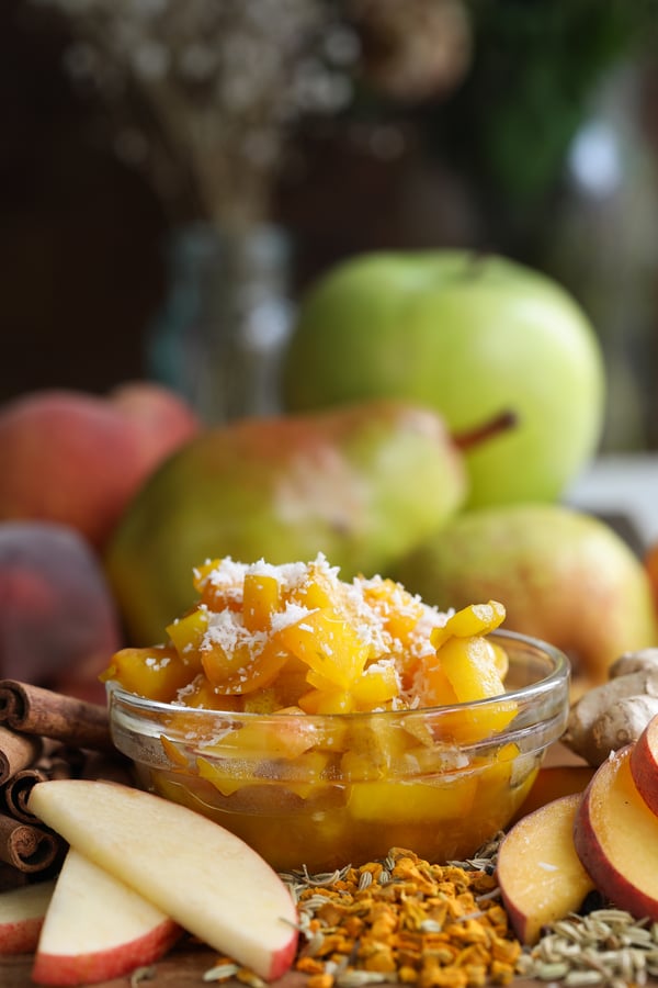 Fruit compote with carminative herbs and spices in a bowl surrounded by fall fruits and spices