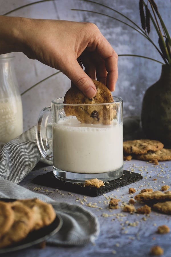 A cookie is dunked into a frothy glass of homemade hemp milk
