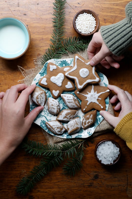 Three hands reaching for a holiday decorated cookie. 