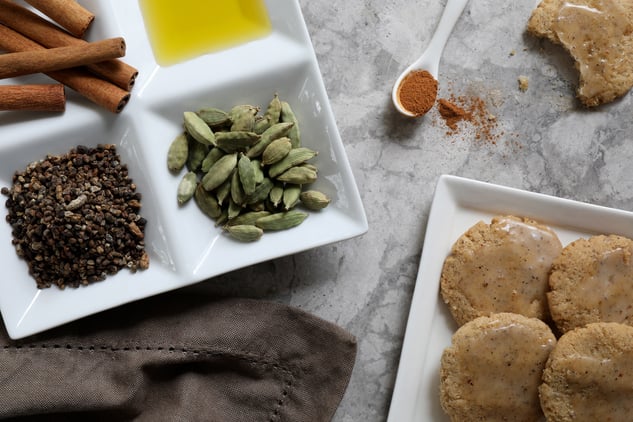 Ingredients for cardamom cookies on counter, plate of cardamom pods, cinnamon sticks, almond  oil