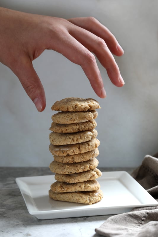 Hand reaching to grab a cardamom cookie from a stack of cookies on a plate