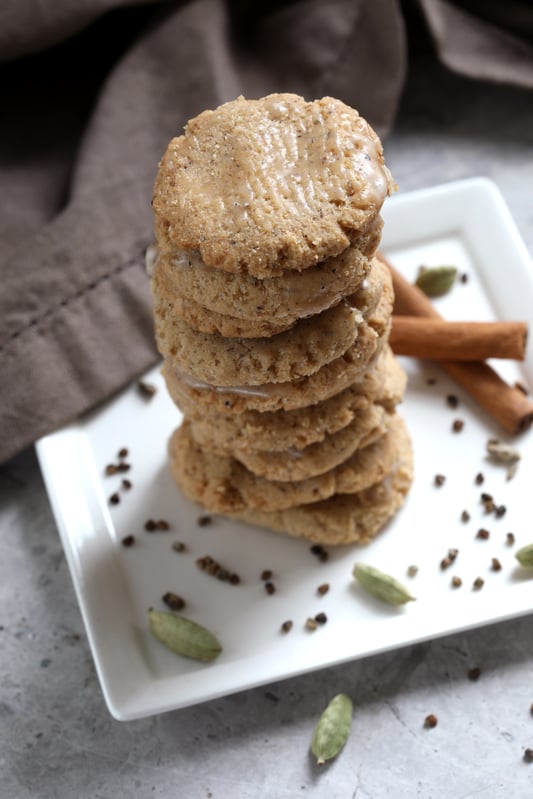 Stack of Cardamom Cookies sprinkled with cardamom powder on a plate with whole herbs 