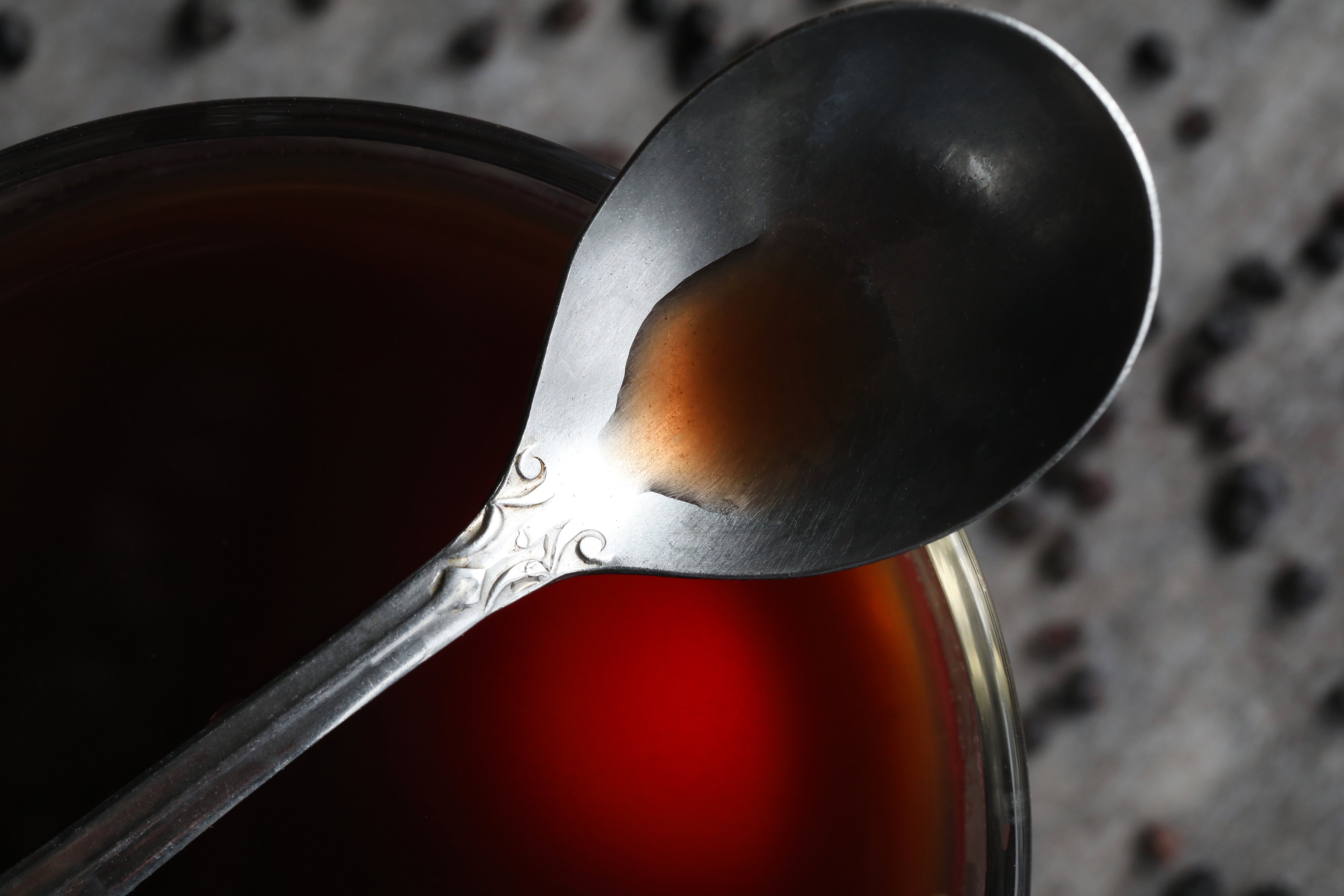 Metal spoon with small amount of deep red syrup.