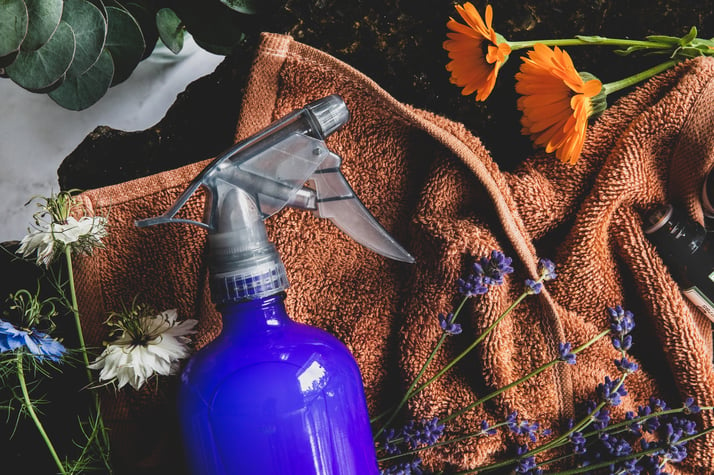 A glass spray bottle filled with cleaner amongst flowers