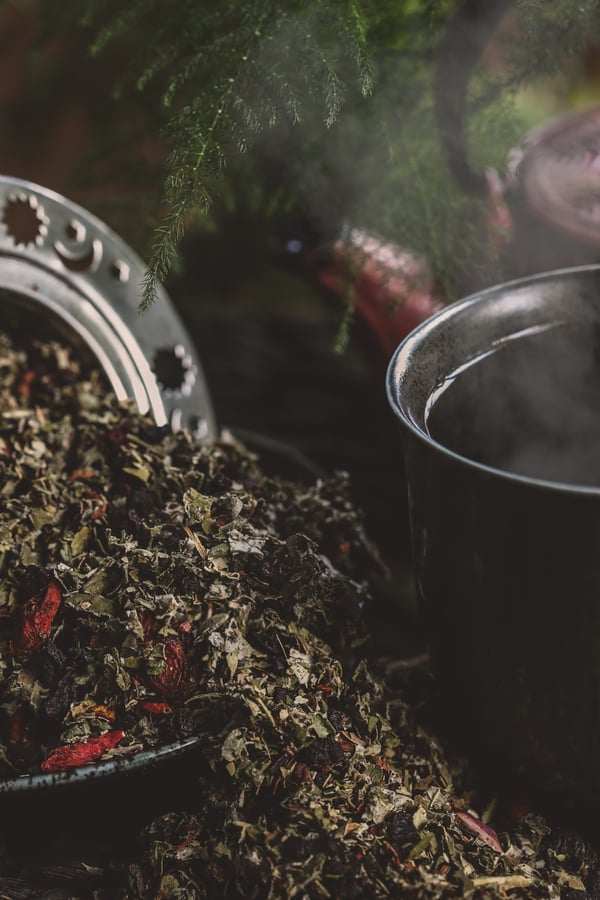 Loose leaf tea spills out from a tea diffuser next to a steamy cup of tea.