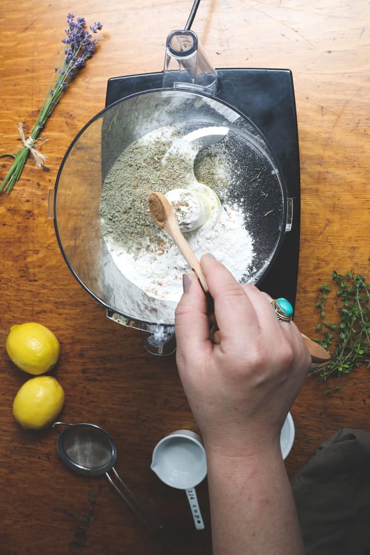 Hand adding spices to food processor with wooden spoon to make lemon bars