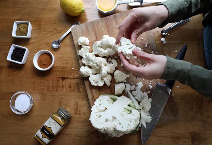 Hands breaking cauliflower into small pieces to make curry cauliflower